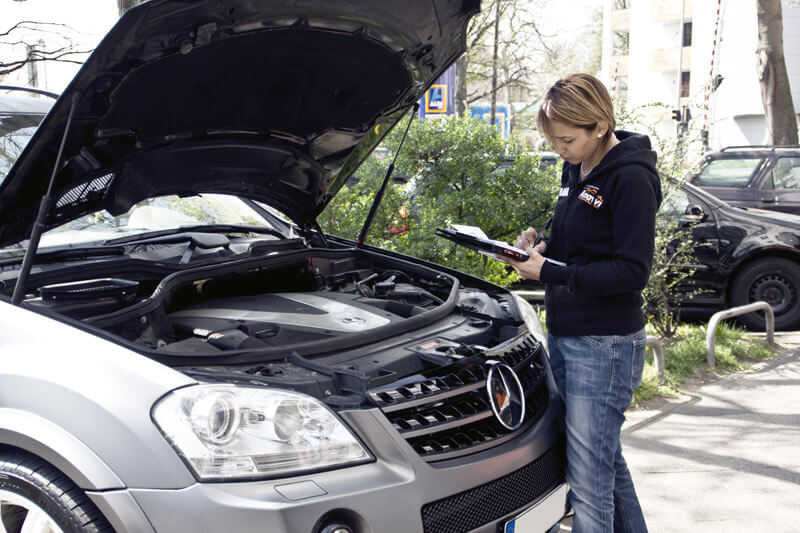 Gebrauchtwagen-Check Gutachterin kontrolliert den Motor eines metallenen Mercedes